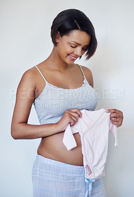 Buy stock photo Studio shot of an attractive young pregnant woman holding pink baby clothes
