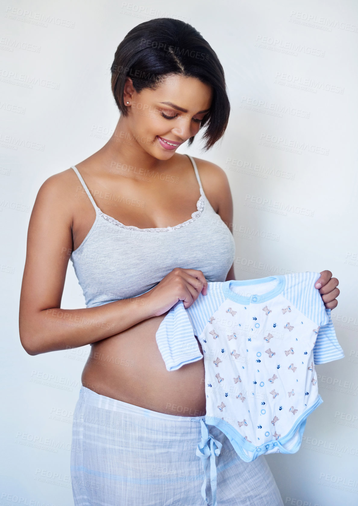 Buy stock photo Studio shot of an attractive young pregnant woman holding blue baby clothes