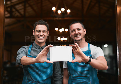 Buy stock photo Portrait of two cheerful businessmen holding up a digital tablet together while standing in front of the doors of a beer brewery