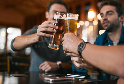 Buy stock photo Shot of three cheerful young men having a celebratory toast with beer while sitting at a table inside of a beer brewery during the day