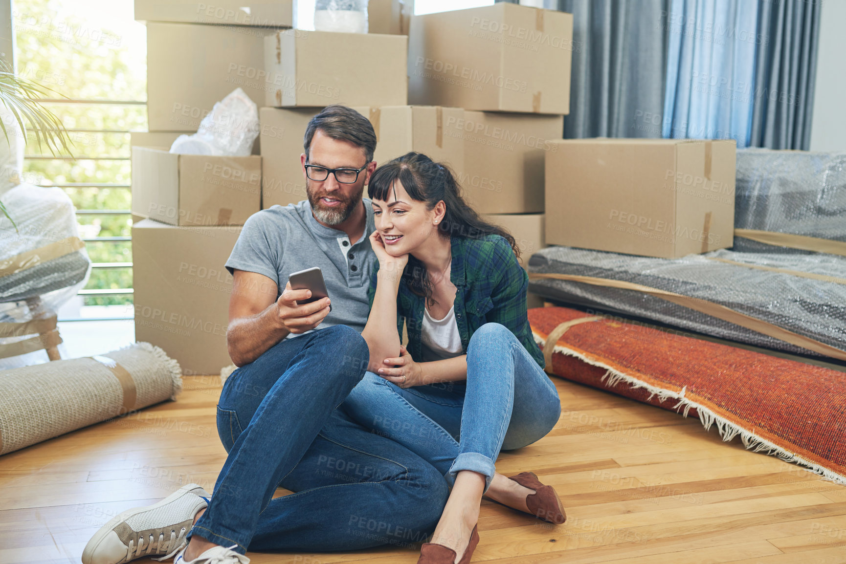 Buy stock photo Shot of a husband and wife using a mobile phone together on moving day