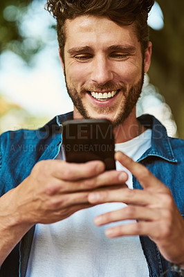 Buy stock photo Shot of a handsome young man using a cellphone outdoors