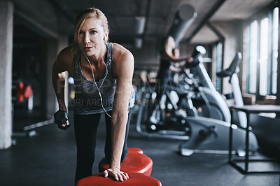 Buy stock photo Cropped shot of an attractive young woman listening to music while working out with a dumbbell in the gym