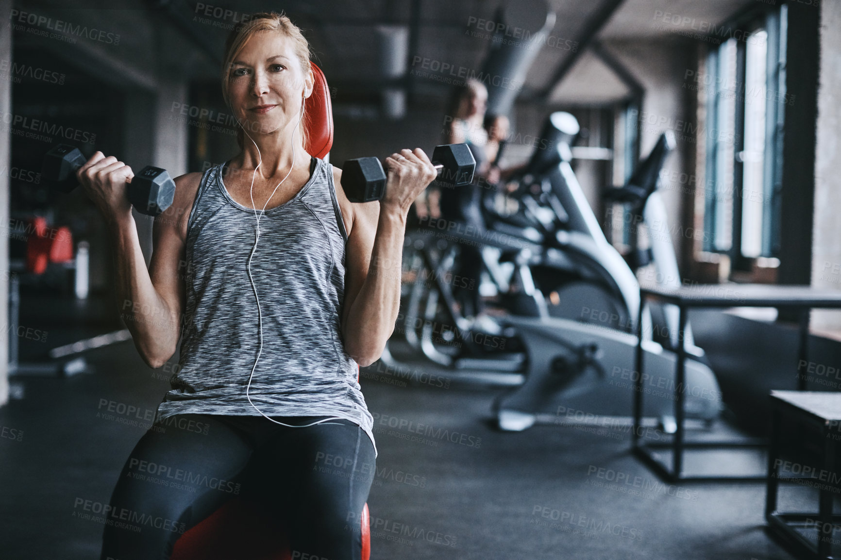 Buy stock photo Cropped shot of an attractive young woman listening to music while working out with dumbbells in the gym