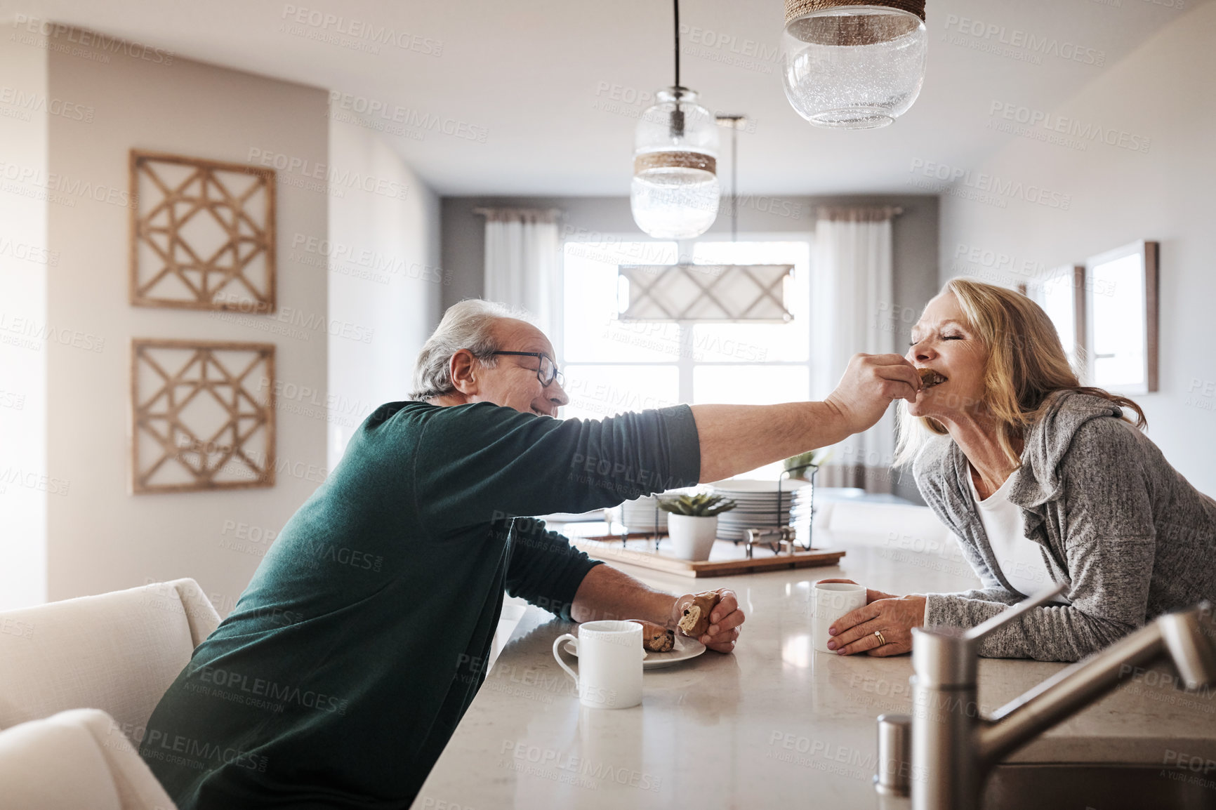 Buy stock photo Shot of a senior man lovingly feeding his wife a taste of his snack during a relaxing day at home