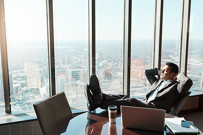 Buy stock photo Shot of a young businessman relaxing with his feet up on a table in an office