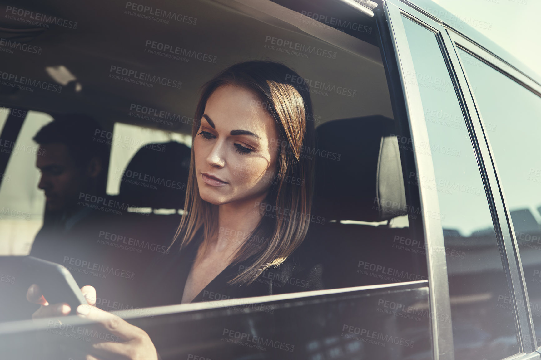 Buy stock photo Shot of a young businesswoman using a mobile phone while traveling in a car