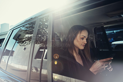 Buy stock photo Shot of a young businesswoman using a mobile phone while traveling in a car