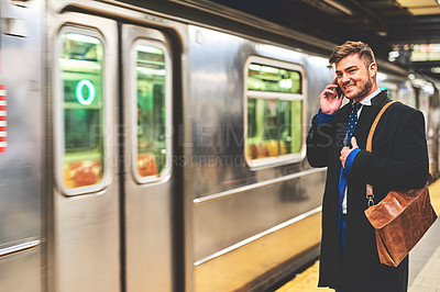 Buy stock photo Shot of a cheerful young man talking on his phone while waiting for a train to get to work in the morning