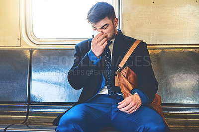 Buy stock photo Shot of a irritated looking young man blowing his nose while being seated inside of a train to get to work