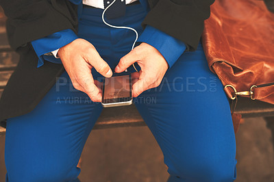 Buy stock photo Shot of an unrecognizable man listening to music while being seated on a bench outside in the morning