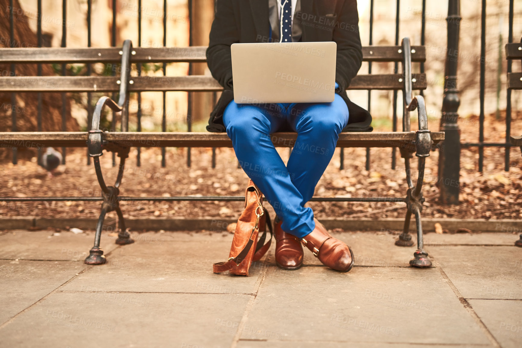 Buy stock photo Shot of an unrecognizable man working on his laptop while being seated on a bench outside during the day