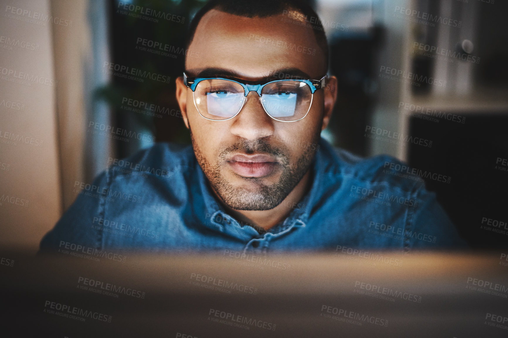 Buy stock photo Shot of a young businessman using a computer during a late night at work in a modern office