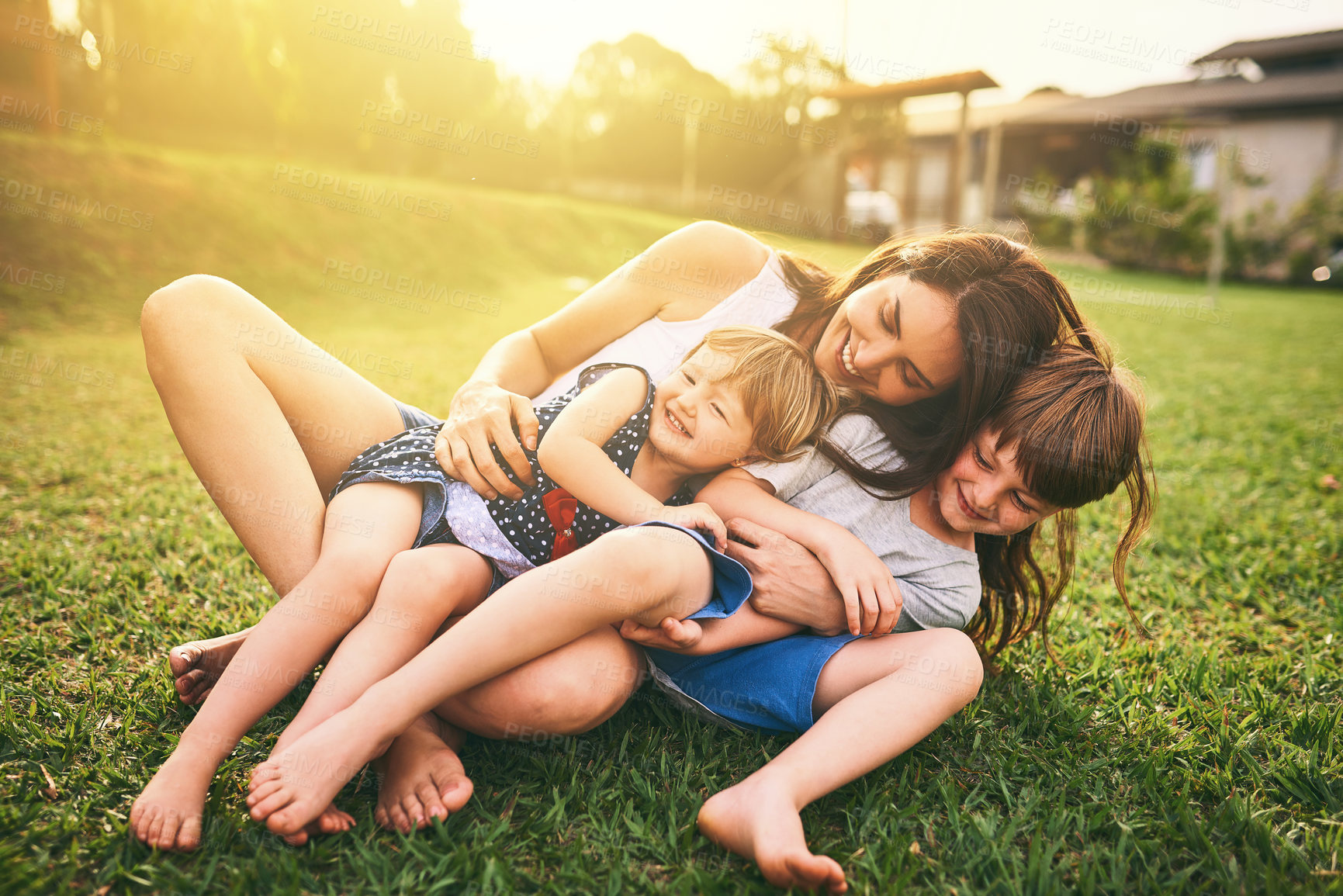Buy stock photo Mother, children and hug playing on grass for fun bonding in the sun outside their house in nature. Happy mom hugging kids on garden floor outdoors in playful, joy and happiness of family together