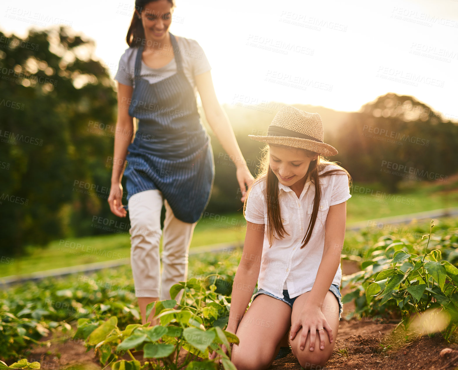 Buy stock photo Shot of a young girl working on the family farm with her mother in the background