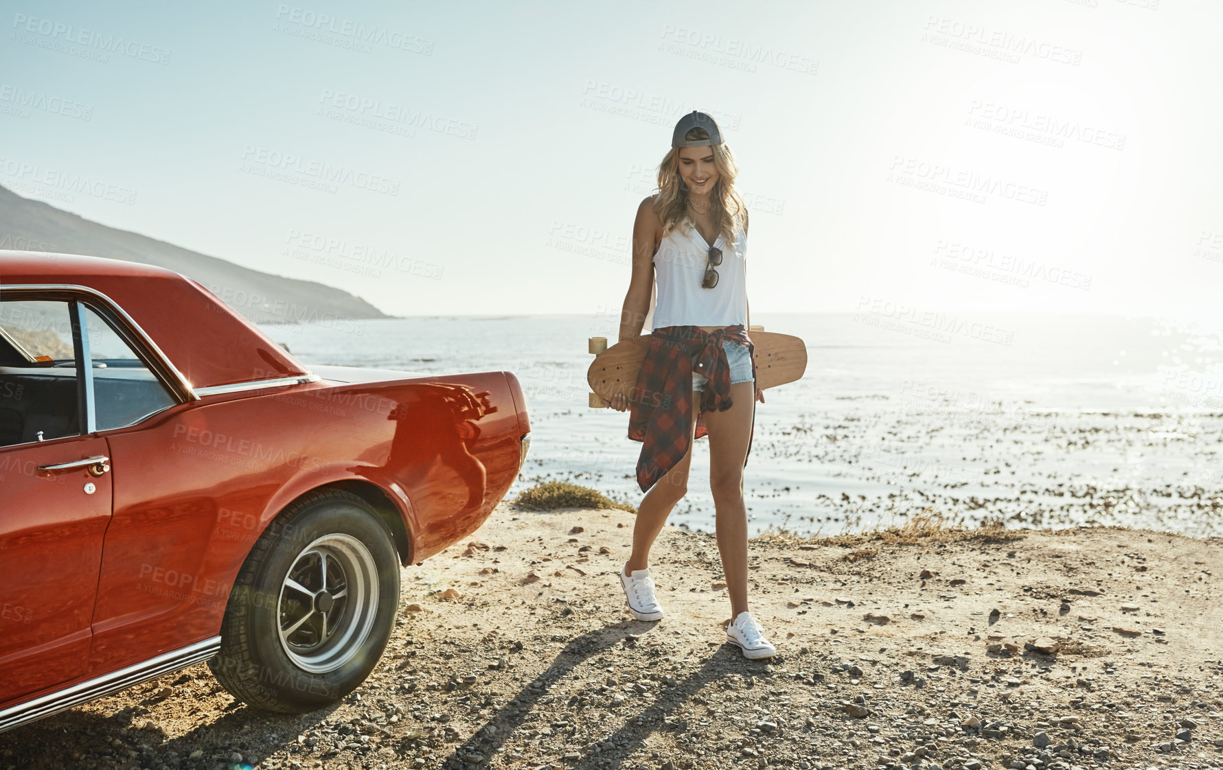 Buy stock photo Shot of an attractive young woman holding a skateboard while on a road trip
