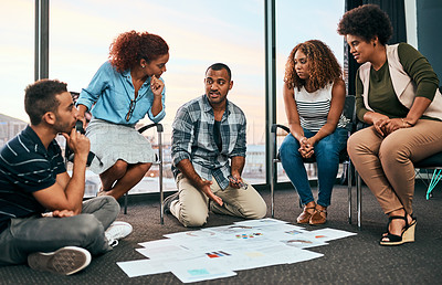 Buy stock photo Shot of a group of focussed young coworkers working together and brainstorming while being seated on the floor of the office at work during the day
