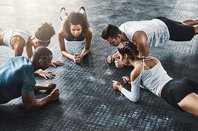 Buy stock photo Shot of a group of young people doing planks together during their workout in a gym