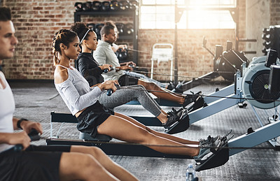 Buy stock photo Shot of a group of young people working out with rowing machines in the gym