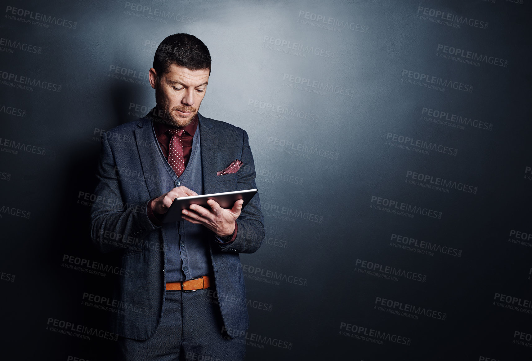 Buy stock photo Cropped shot of a handsome young businessman using his tablet while standing against a dark background