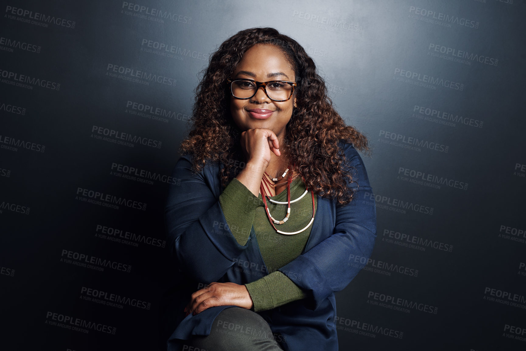 Buy stock photo Cropped portrait of an attractive young businesswoman sitting with her hand on her chin against a dark background