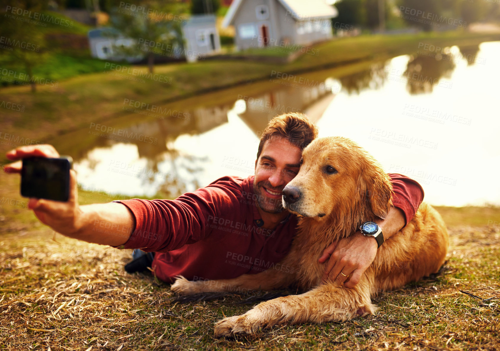 Buy stock photo Full length shot of a handsome young man and his dog taking selfies by a lake in the park