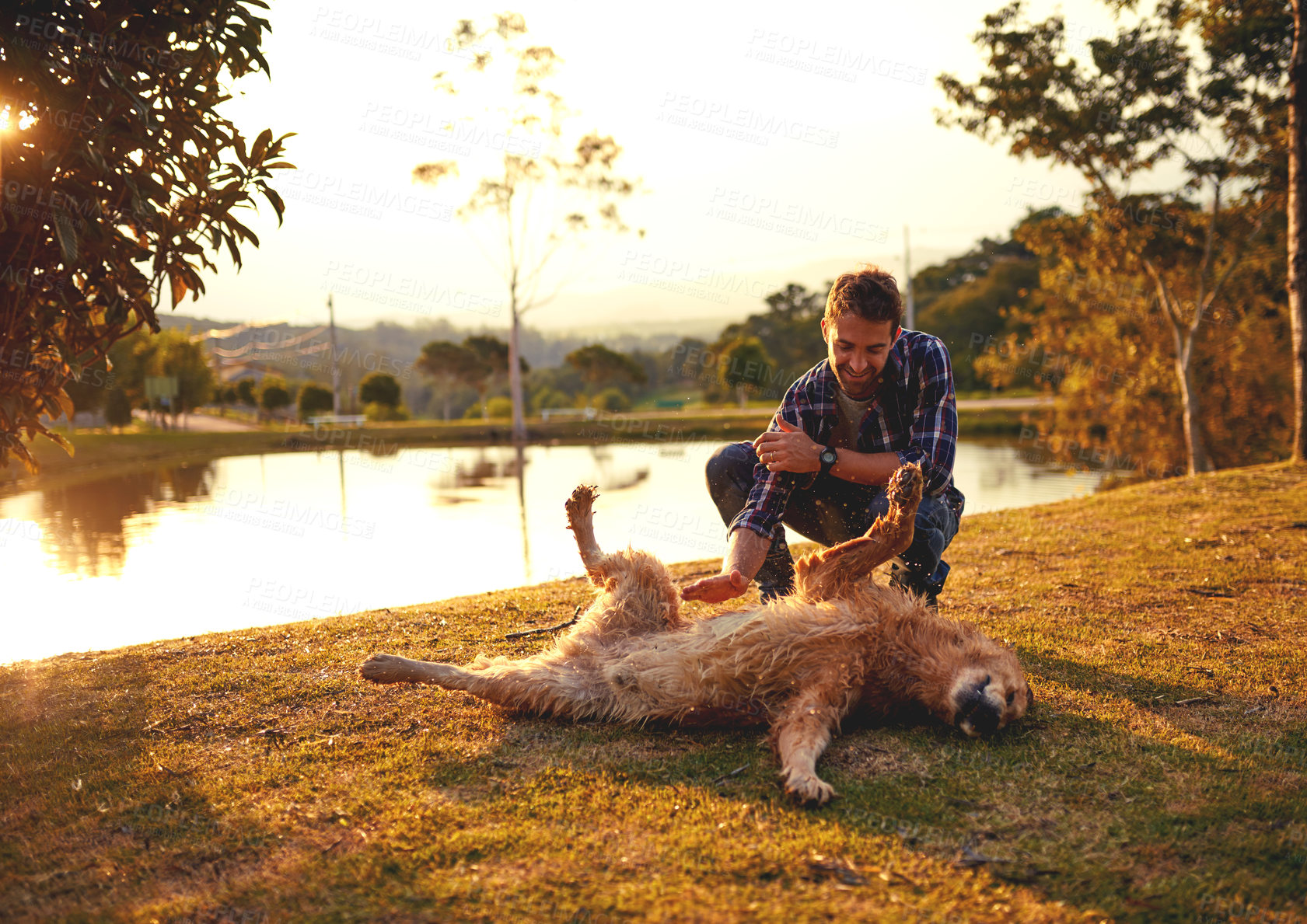 Buy stock photo Full length shot of a handsome young man playing with his dog by a lake in the park