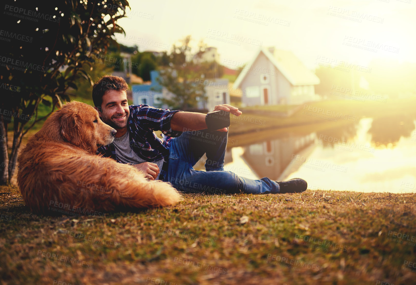 Buy stock photo Full length shot of a handsome young man and his dog taking selfies by a lake in the park