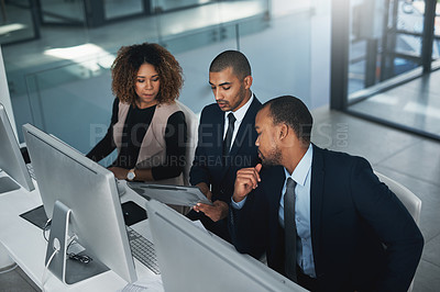 Buy stock photo High angle shot of three corporate businesspeople looking over some paperwork in their office