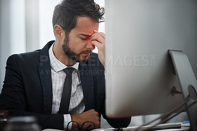 Buy stock photo Shot of a young businessman suffering with a headache while working in an office