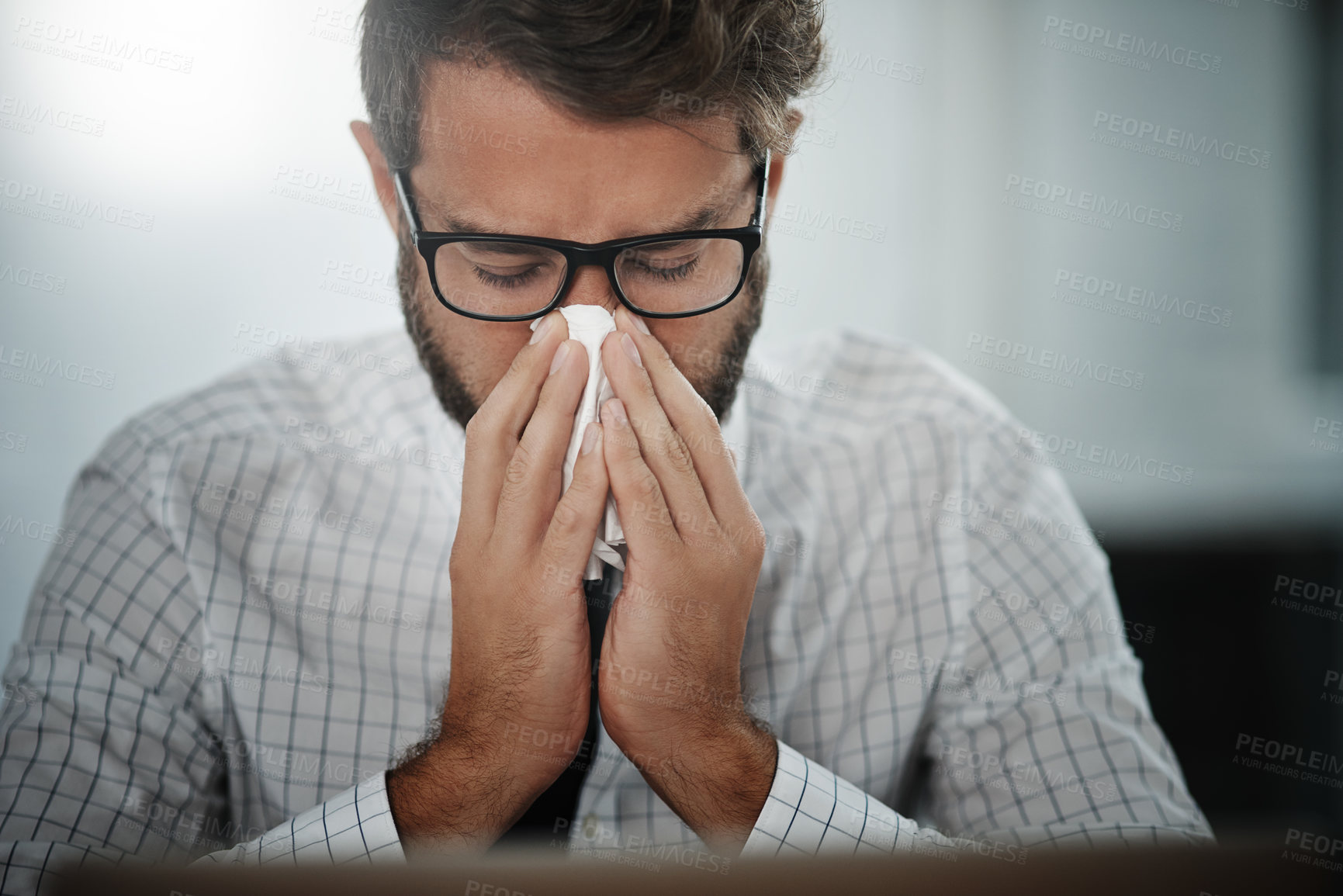 Buy stock photo Shot of a young businessman blowing his nose in an office