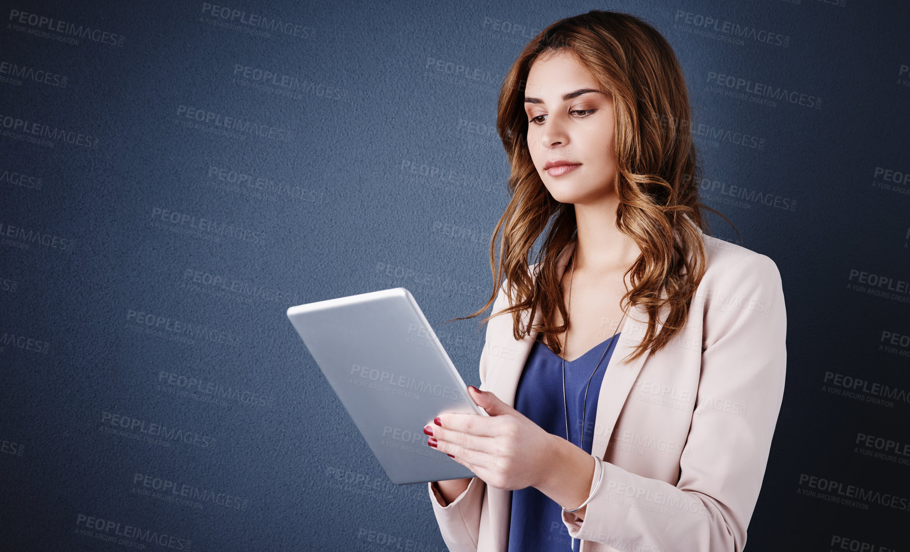 Buy stock photo Studio shot of an attractive young businesswoman using a digital tablet against a dark blue background