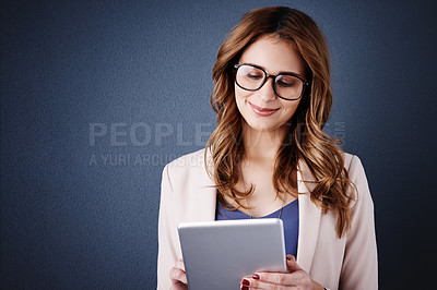 Buy stock photo Studio shot of an attractive young businesswoman using a digital tablet against a dark blue background