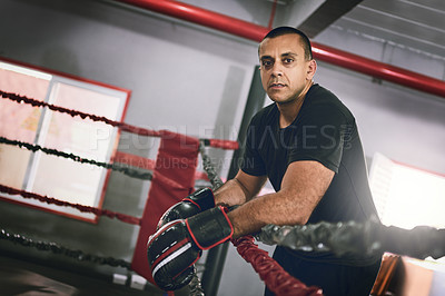 Buy stock photo Portrait of a confident young male boxer leaning against ropes inside of a boxing ring at a gym during the day
