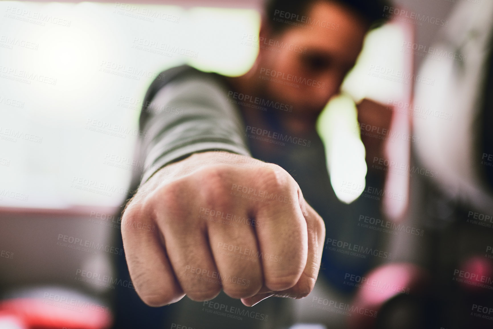 Buy stock photo Closeup of a focused young male boxer throwing punches at the camera inside of a ring at a gym during the day