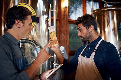 Buy stock photo Shot of two focused young male business owners testing out a fresh batch of beer inside of their beer brewery during the day