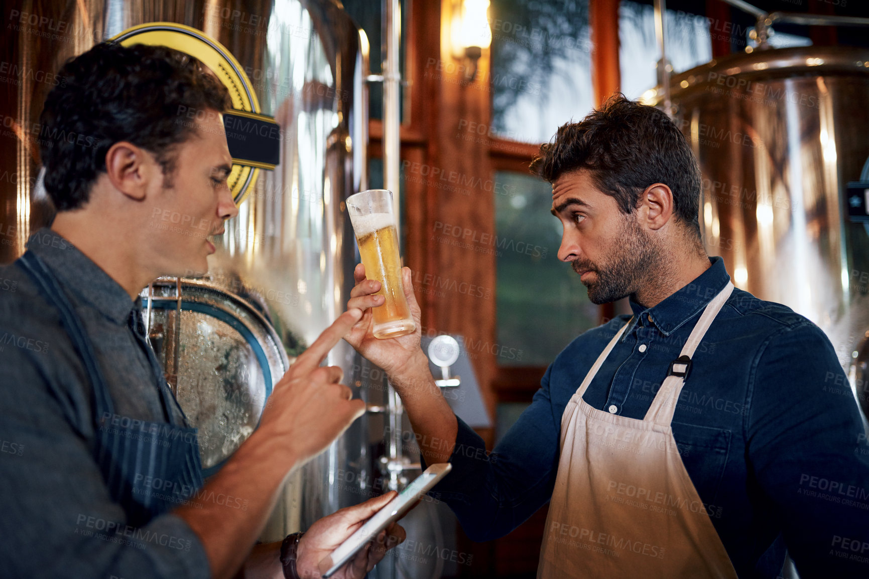 Buy stock photo Shot of two focused young male business owners testing out a fresh batch of beer inside of their beer brewery during the day