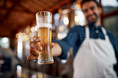 Buy stock photo Closeup of a cheerful young business owner holding up a glass of beer that he just poured inside of a beer brewery during the day