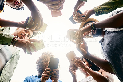 Buy stock photo Low angle shot of a group of friends using cellphones in a public park