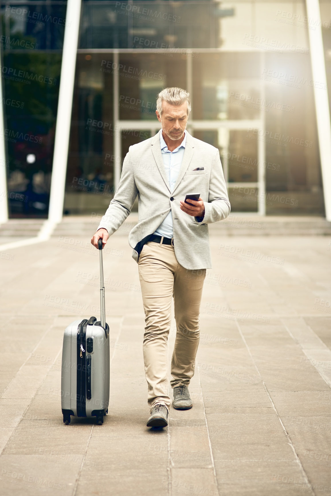 Buy stock photo Shot of a mature businessman using a cellphone while walking with a suitcase in the city