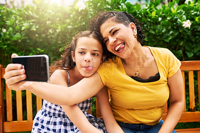 Buy stock photo Cropped shot of a young mother and her daughter taking selfies while sitting on a bench in the park