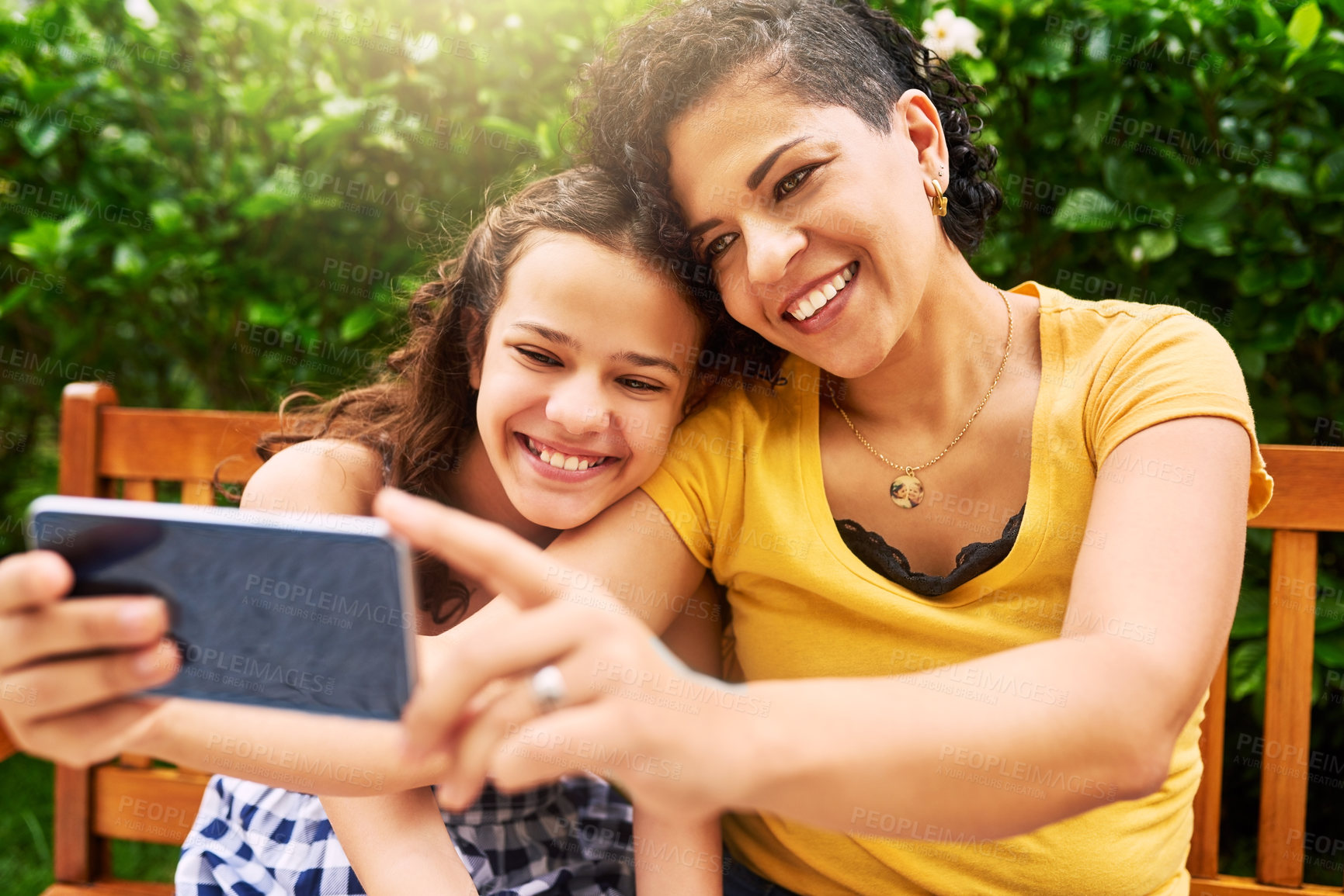 Buy stock photo Cropped shot of a young mother and her daughter taking selfies while sitting on a bench in the park