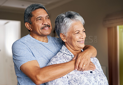 Buy stock photo Shot of a cheerful mature couple holding each other while looking outside through a window at home during the day
