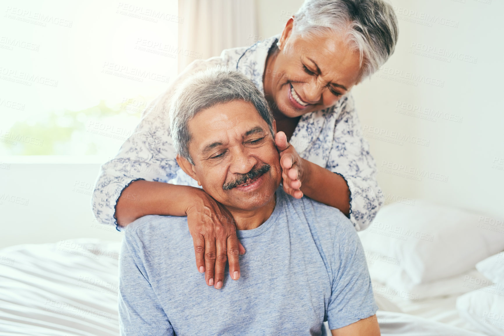 Buy stock photo Shot of a cheerful mature couple holding each other while being seated on a bed at home during the day