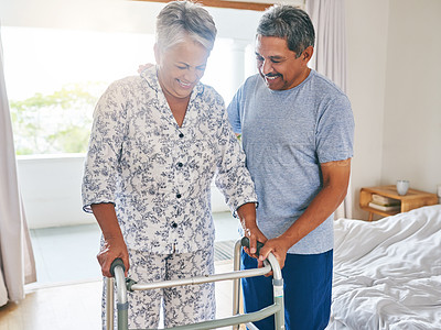 Buy stock photo Shot of a determined mature woman using a walking frame to walk with while being supported by her husband at home during the day