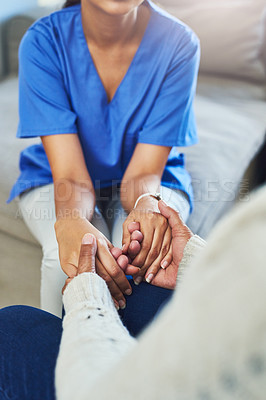 Buy stock photo Shot of an unrecognizable female nurse holding a patient's hands in support while being seated on a couch at home during the day