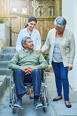 Buy stock photo Shot of a cheerful elderly man seated in a wheelchair while being supported by his wife and a female nurse at home during the day