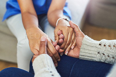 Buy stock photo Shot of an unrecognizable female nurse holding a patient's hands in support while being seated on a couch at home during the day