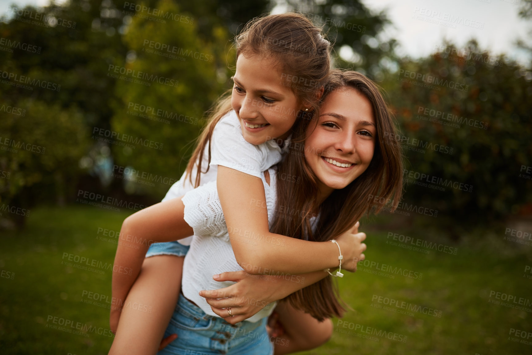 Buy stock photo Cropped portrait of a young girl giving her younger sister a piggyback ride outdoors