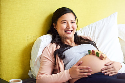 Buy stock photo Portrait of a pregnant woman lying down with wooden baby blocks on her belly at home
